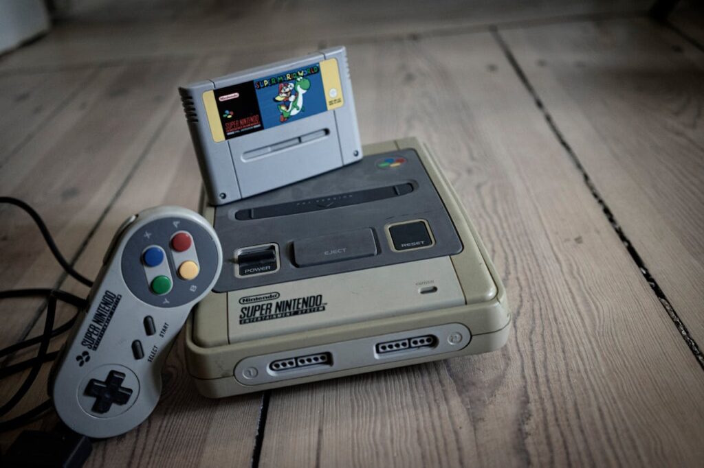 From above of aged video game console with cassette and controller with colorful buttons on wooden surface